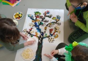 Uczniowie ozdabiają swoje namalowane farbami wiosenne drzewo